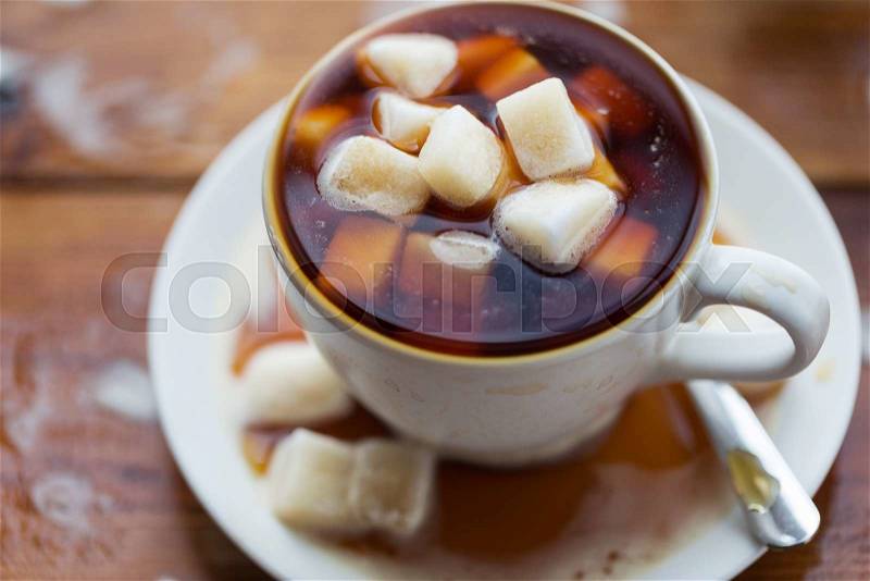 Unhealthy eating, object and drinks concept - close up of lump sugar heap drowned in cup of coffee on wooden table, stock photo