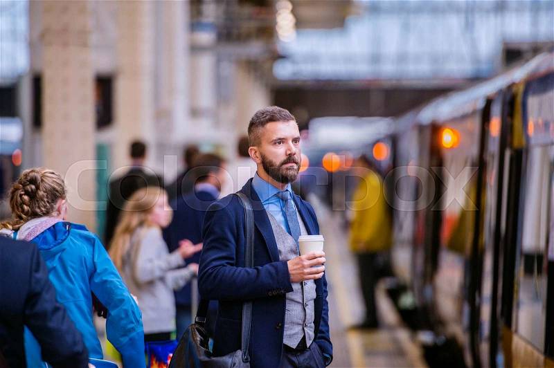 Hipster businessman holding a disposable coffee cup at the train station platform, stock photo