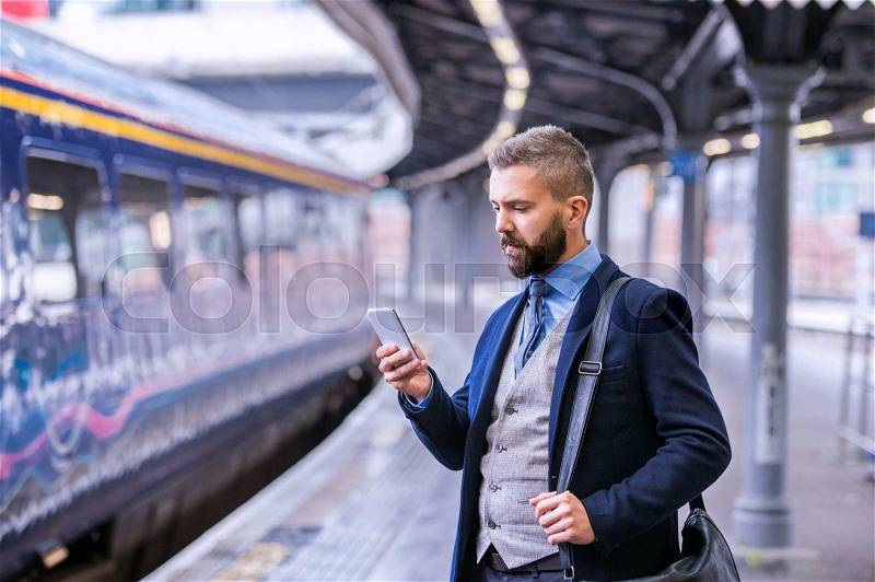 Hipster businessman with smartphone, waiting at the train station platform, stock photo