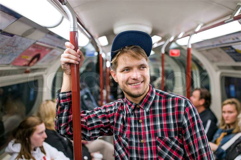 Young hipster man in checked shirt standing in a crowded subway train, stock photo