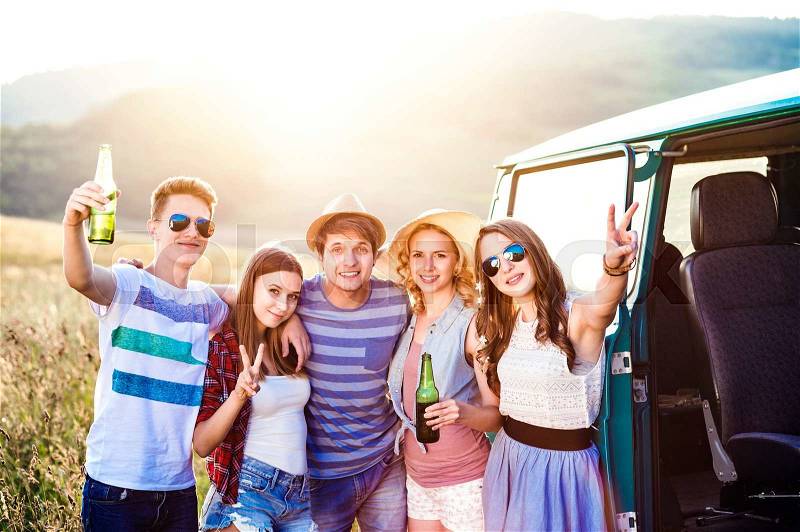 Group of teenage hipsters on a roadtrip, drinking beer. Young friends outside on a summer day, stock photo