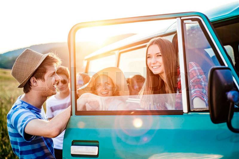 Group of teenage hipsters on a roadtrip having fun, standing at the campervan. Young friends outside on a summer day, stock photo