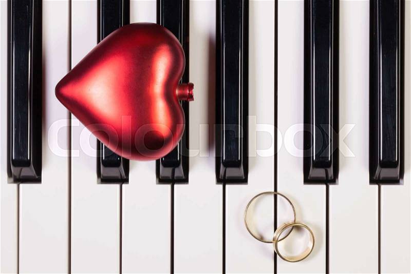 Detail of piano keyboard ,red heart and wedding rings, stock photo
