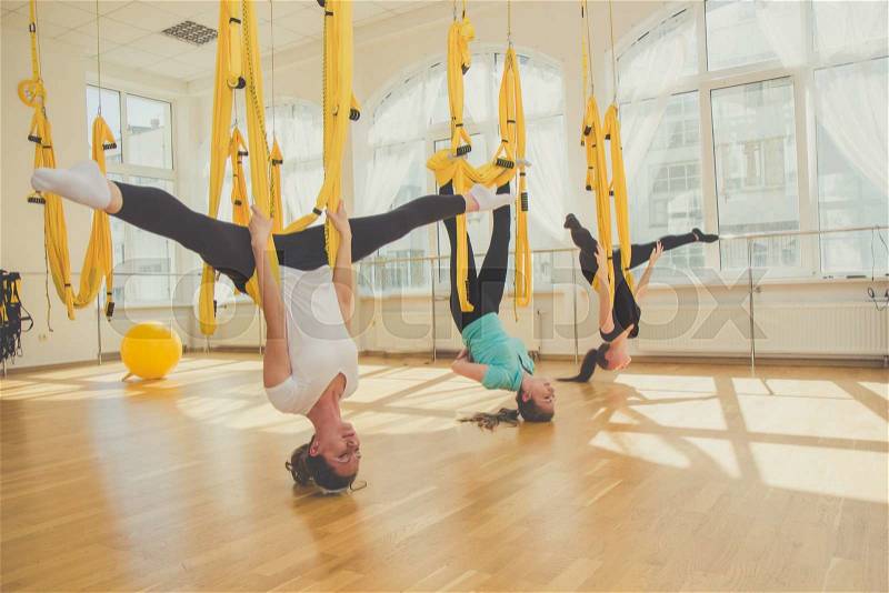 Young slim women doing aerial fly yoga exercise or antigravity yoga in fitness studio. Flying, fitness, balance, exercise and healthy lifestyle people. Woman using yellow hammocks for stretching, stock photo