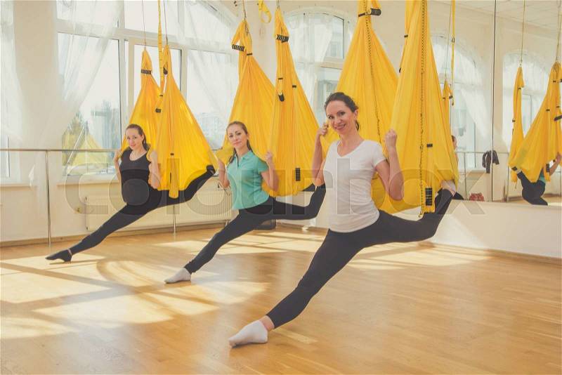 Young slim women doing aerial yoga exercise or antigravity yoga in fitness studio. Flying, fitness, stretch, balance, exercise and healthy lifestyle people. Woman using yellow hammocks for stretching, stock photo