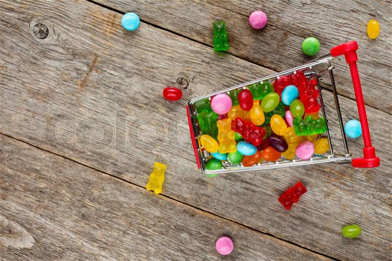 Shopping cart full of candies on a wooden background, stock photo