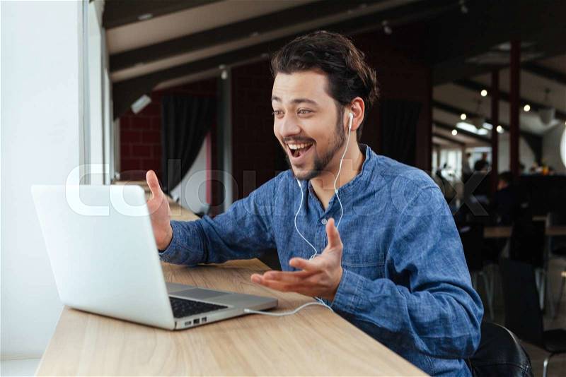 Cheerful man video chatting on laptop computer in office, stock photo