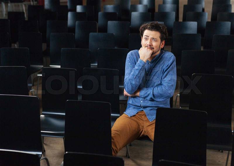 Scared man in casual cloth sitting in conference hall, stock photo