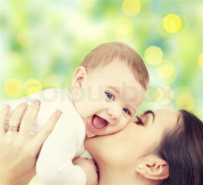 People, family, motherhood and children concept - happy mother hugging adorable baby over green lights background, stock photo