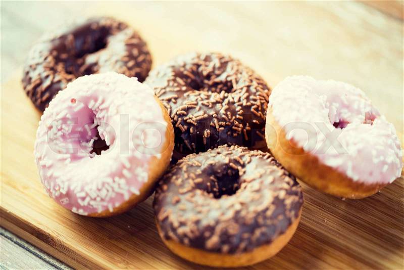 Food, junk-food and eating concept - close up of glazed donuts on wooden board, stock photo