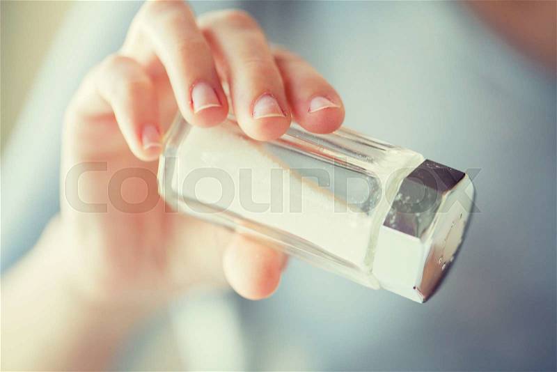 Food, junk-food, cooking and unhealthy eating concept - close up of hand holding white salt cellar, stock photo