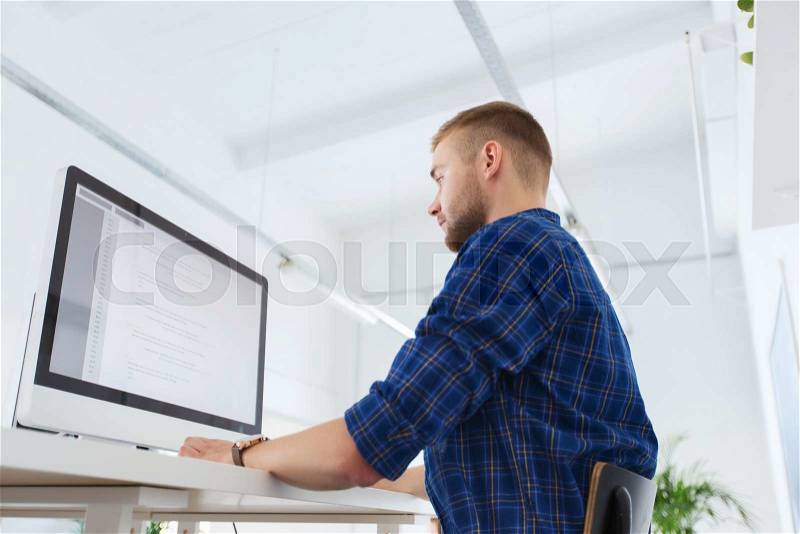Business, technology, education and people concept - young creative man or programmer with computer working at office, stock photo