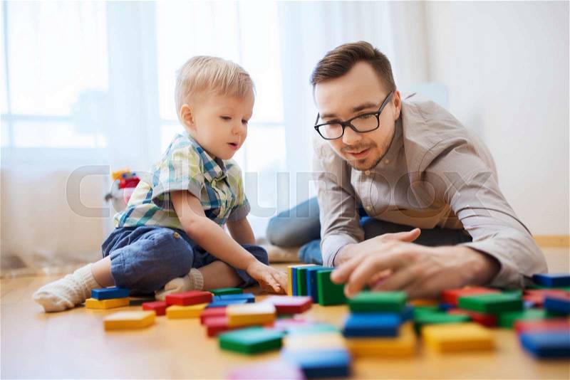 Family, childhood, creativity, activity and people concept - happy father and little son playing with toy blocks at home, stock photo