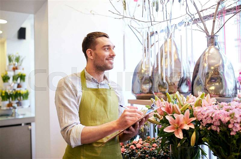 People, sale, retail, business and floristry concept - happy smiling florist man with clipboard writing and making notes order at flower shop, stock photo