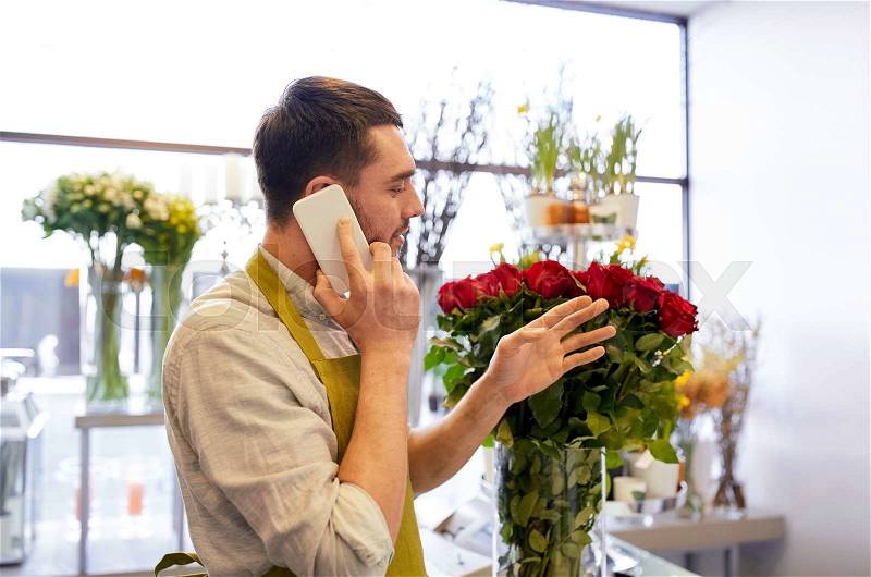 People, sale, retail, business and floristry concept - florist man with red roses calling on smartphone at flower shop counter, stock photo