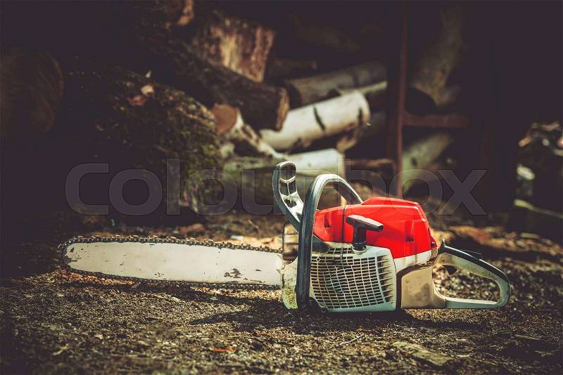 Gasoline Wood Cutter Works. Wood Cutting Gasoline Power Tool and Wood Logs in the Background, stock photo