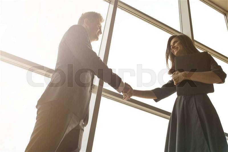 Business men and women shaking hands with a smile on the background of the large panoramic windows in a modern business center. Models dressed in a dark business suits, stock photo