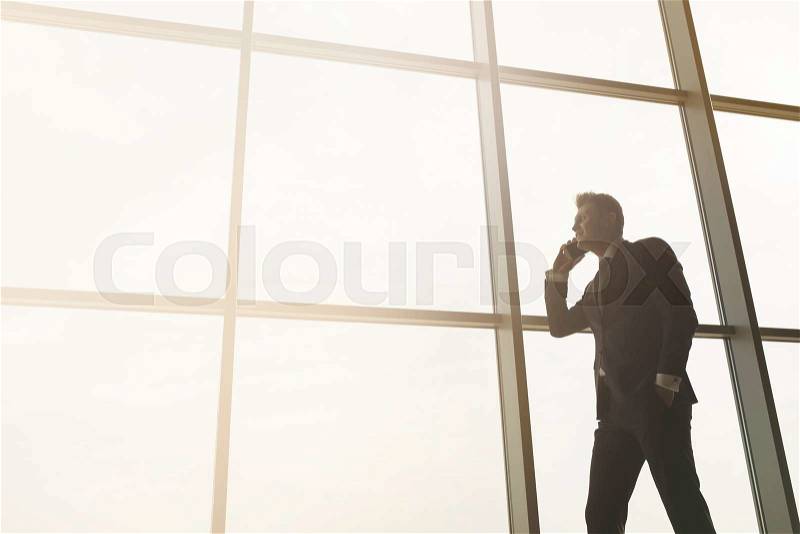 Stylish business man in the background of a large window in the floor. Model talking on the phone, stock photo