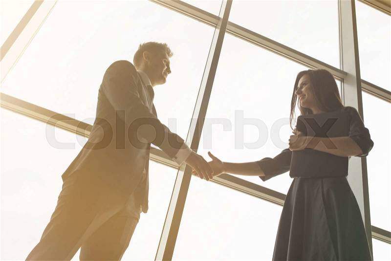 Business men and women shaking hands with a smile on the background of the large panoramic windows in a modern business center. Models dressed in a dark business suits, stock photo