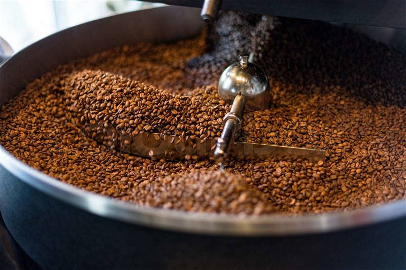 The freshly roasted coffee beans from a large coffee roaster in the cooling cylinder. Motion blur on the beans, stock photo