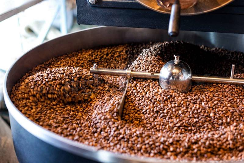 The freshly roasted coffee beans from a large coffee roaster in the cooling cylinder. Motion blur on the beans, stock photo