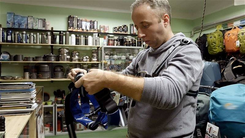 Man chooses and selects tackle outfit alpinist climber mountaineer equipment in the tourist travel shop for sport caving in speleological training and mountain hiking climbing. , stock photo