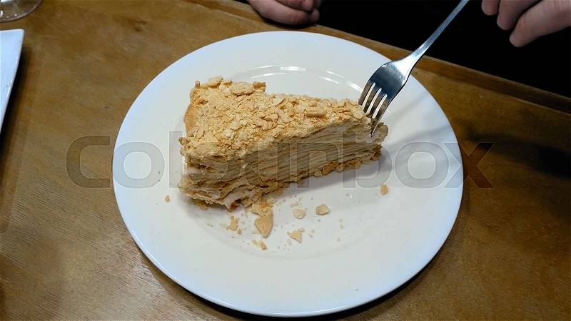 Piece of creamy sweet cake being cut with fork on white plate and eaten in a cafe restaurant. Close up shot. , stock photo