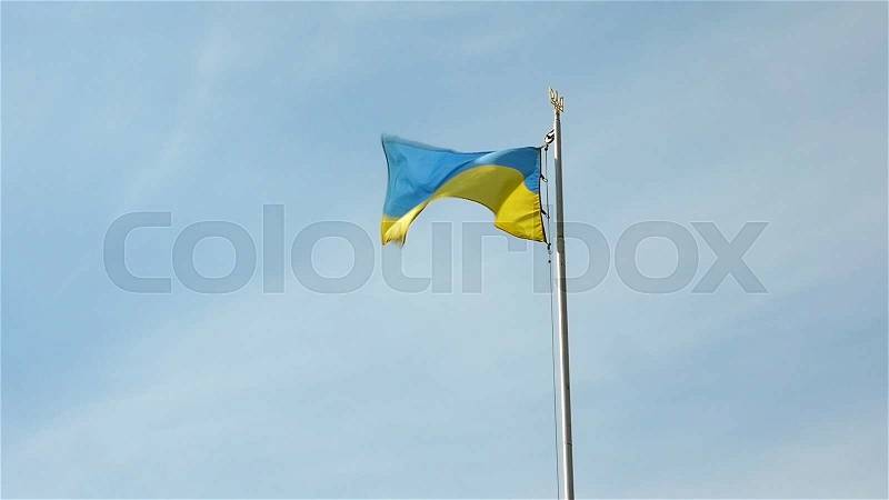 Ukrainian national flag banner flying and waving in the wind on flagpole with coat of arms, stock photo