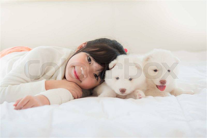 Little asian girl lying with two siberian husky puppies on bed, stock photo