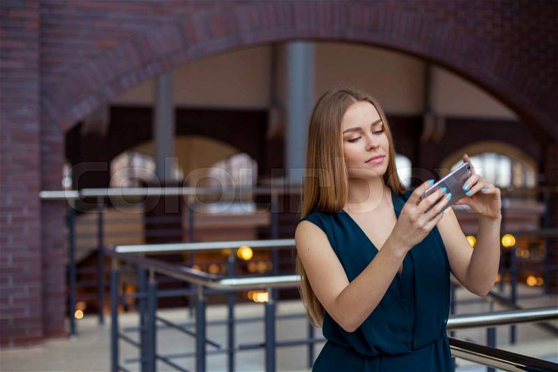 Photo of beautiful young business woman standing in office. Woman with blue shirt making selfie with mobile phone, stock photo