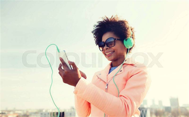 Technology, lifestyle and people concept - smiling african american young woman or teenage girl with smartphone and headphones listening to music outdoors, stock photo