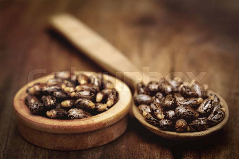 Castor beans in a wooden spoon and bowl on wooden surface, stock photo