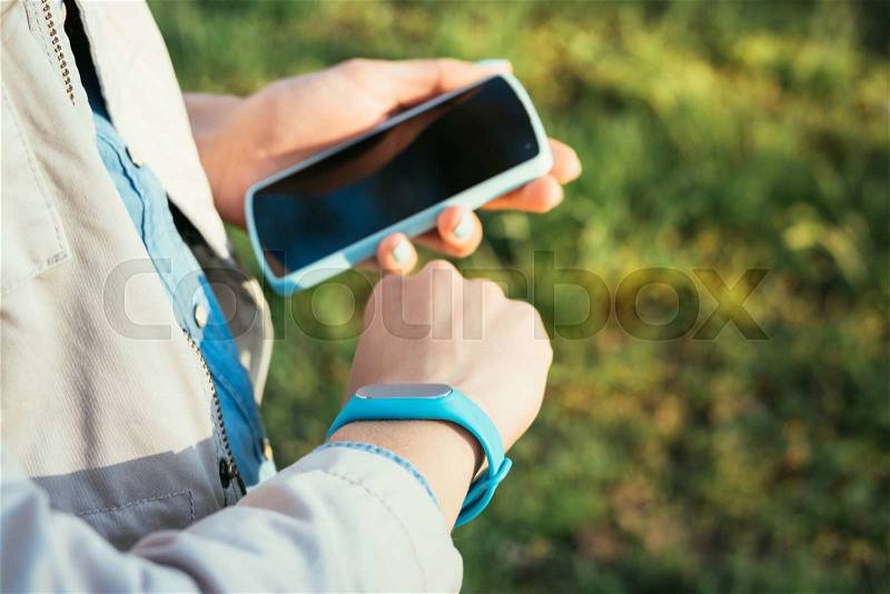 Woman checks data from fitness bracelet on a mobile phone while walking in the park, stock photo