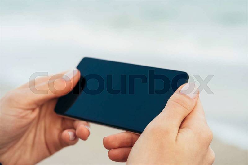 Female hands holding phone with touch screen on the background of the sea. Shallow depth of field, stock photo