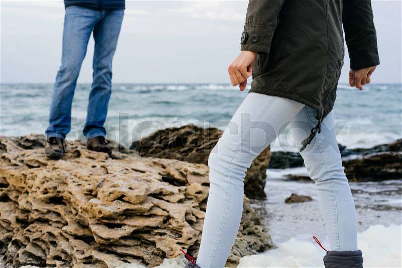 Female and male feet in jeans on the rocky coast in cloudy day, stock photo
