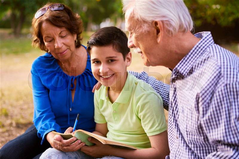 Grandparents educating grandson: Senior woman and old man spending time with their grandchild in park. The old people help the preteen boy doing his school homework. The kid looks at camera, stock photo
