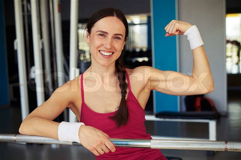 Smiling woman show her biceps in sport club and holding on to the rod in sport club, stock photo