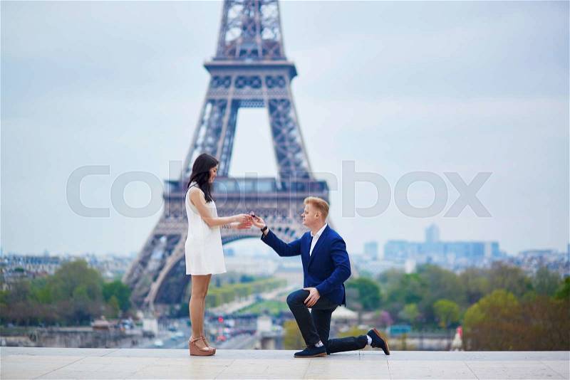 Romantic engagement in Paris, man proposing to his beautiful girlfriend near the Eiffel tower. Surprise proposal or elopement concept, stock photo