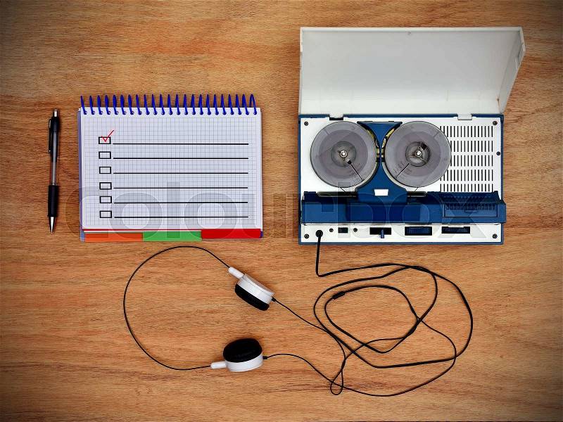 Reel tape recorder with headphones. Notepad with check box on wooden table. View from above, stock photo