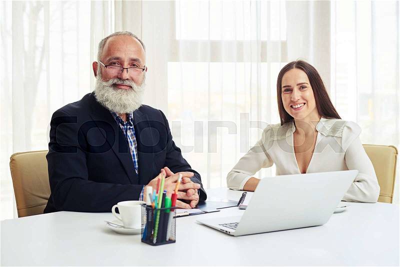 Portrait of smiling young businesswoman and senior man with beard in meeting, stock photo