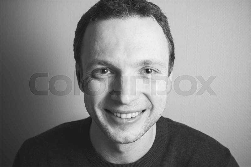 Young handsome smiling man, portrait over gray wall background, black and white photo, stock photo