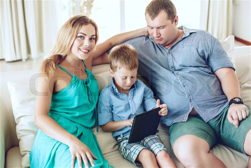 Happy family resting on a sofa and using digital tablet together in living room, stock photo