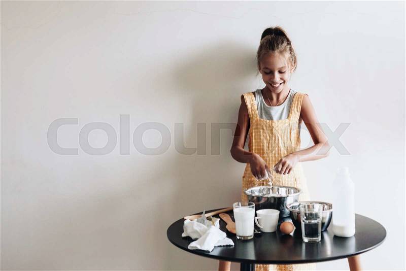 10 years old preteen girl dressed in cotton apron is cooking holiday pie on the table over wall, organic food, lifestyle photo, stock photo