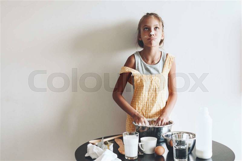 10 years old preteen girl dressed in cotton apron is cooking holiday pie on the table over wall, organic food, lifestyle photo, stock photo