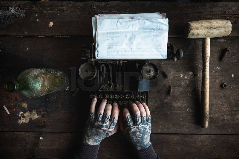Writer with tattooed hand writing on old typing machine with blank paper,selective focus , stock photo