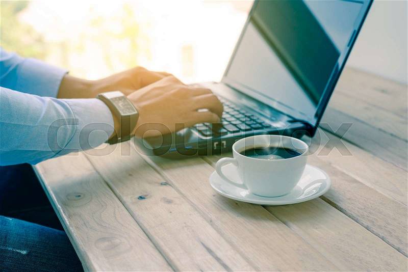 Coffee cup with closeup man typing a laptop on wooden table. , stock photo
