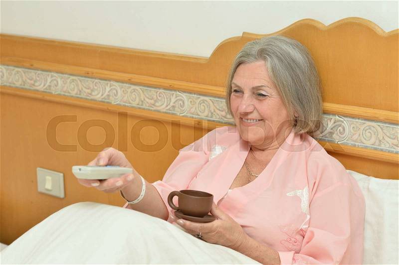 Senior woman in bedroom with cup of coffee, stock photo