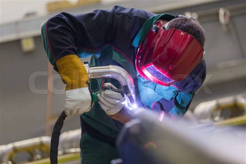 Industrial worker with protective mask welding inox elements in steel structures manufacture workshop, stock photo