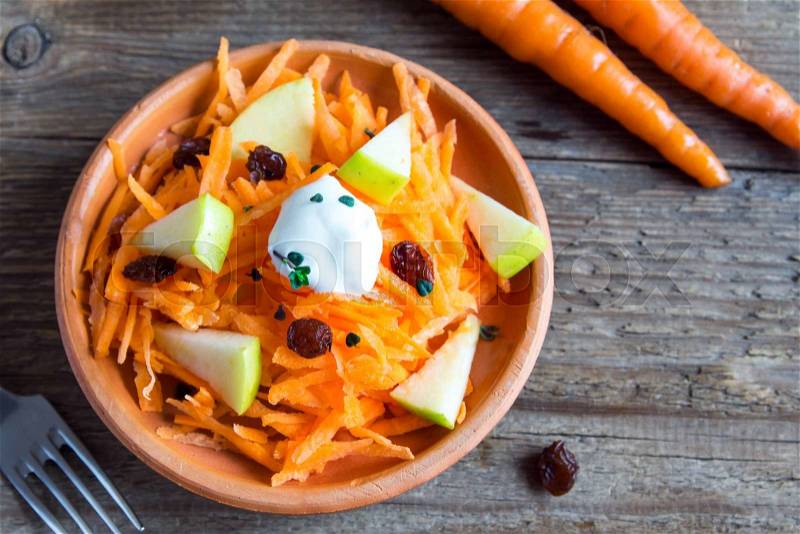 Carrot and apple salad with raisins, yogurt and herbs in rustic ceramic bowl, copy space, stock photo
