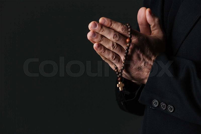 Hands of priest holding rosary and praying over black background, stock photo